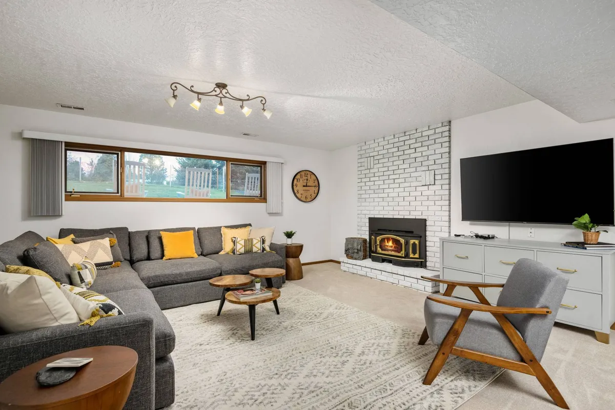 A welcoming living room featuring a comfortable sofa accented with yellow cushions, a roaring fireplace, a large television, and a wooden coffee table. The room is bathed in natural light, creating a cozy ambiance ideal for relaxing, watching movies, or gathering as a group during colder months.