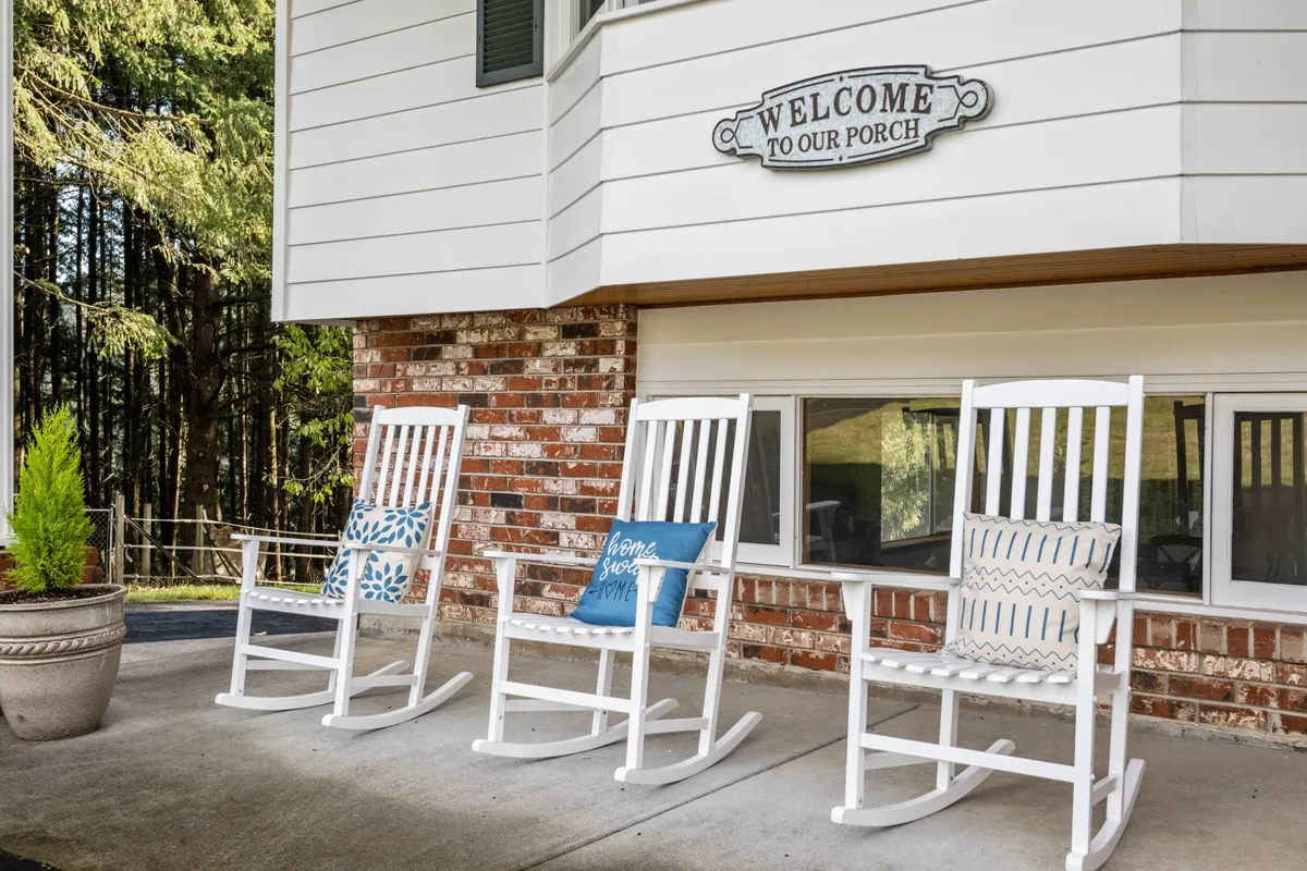 This exterior image captures the inviting front porch with classic rocking chairs, a cheerful welcome sign, and lush potted plant. The scene radiates a sense of arrival and community, hinting at the outdoor possibilities and shared spaces the estate offers.
