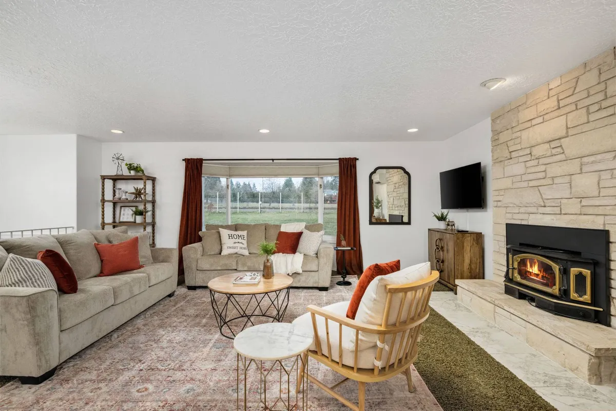 A spacious living room featuring a stone fireplace, comfortable sofa with decorative throw pillows, a stylish coffee table, and a large window offering scenic views. The warm, welcoming decor immediately sets the tone for communal relaxation and togetherness.
