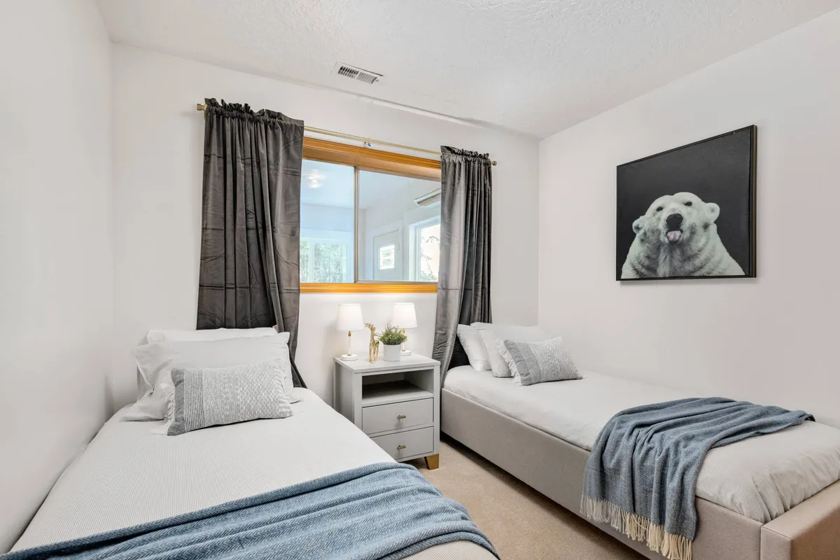A cozy twin bedroom is shown, with two twin beds, playful polar bear artwork, a nightstand with lamp, and tranquil lighting. The decor suggests a comfortable and welcoming space, suitable for children or extra guests.