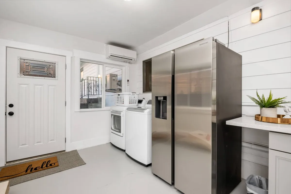 An image showing the welcoming entrance of the home, featuring the front door, refrigerator, washer and dryer, and a touch of greenery. The space is clean and organized, with easy-to-maintain surfaces, creating a pet-friendly atmosphere.