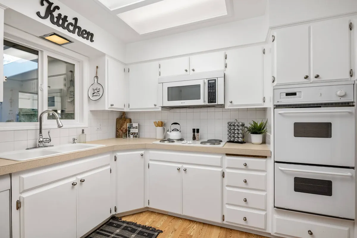 A cheerful, functional kitchen featuring a sink, microwave, stove, and a kitchen sign, set up perfectly for group meal preparation. The space feels inviting and practical for sharing recipes and holiday celebrations.