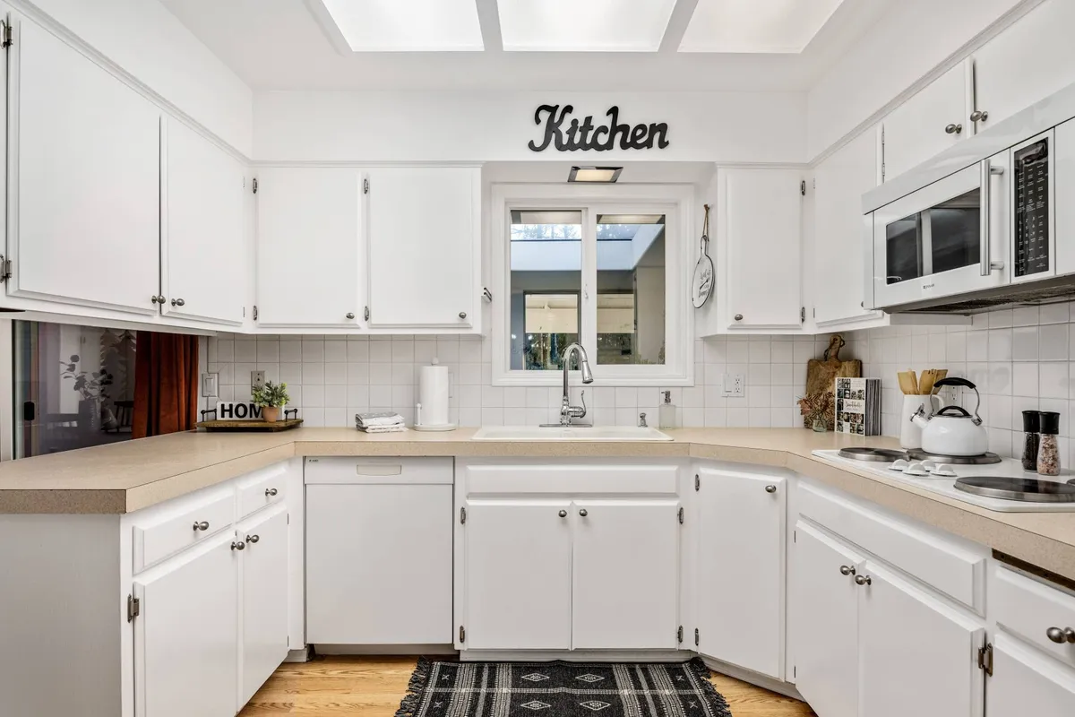 A bright kitchen scene viewed through a window, complete with a sink and inviting countertop. The space is designed for social cooking, baking, and hosting family gatherings, evoking a sense of togetherness and warmth.